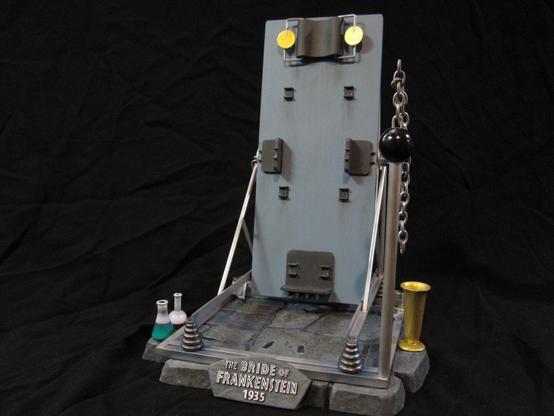 X-Plus bride of Frankenstein model kit. Just the stone base with various metal work and scientific equipment. A black background.