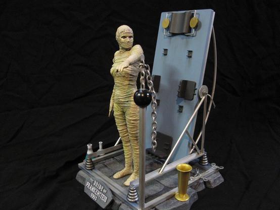 X-Plus bride of Frankenstein model kit. Tan-bandaged Bride. On a stone base with various metal work and scientific equipment. A black background.