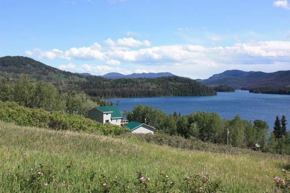 A view of a blue lake nestled in the hills, with a grassland and trees in the foregound.