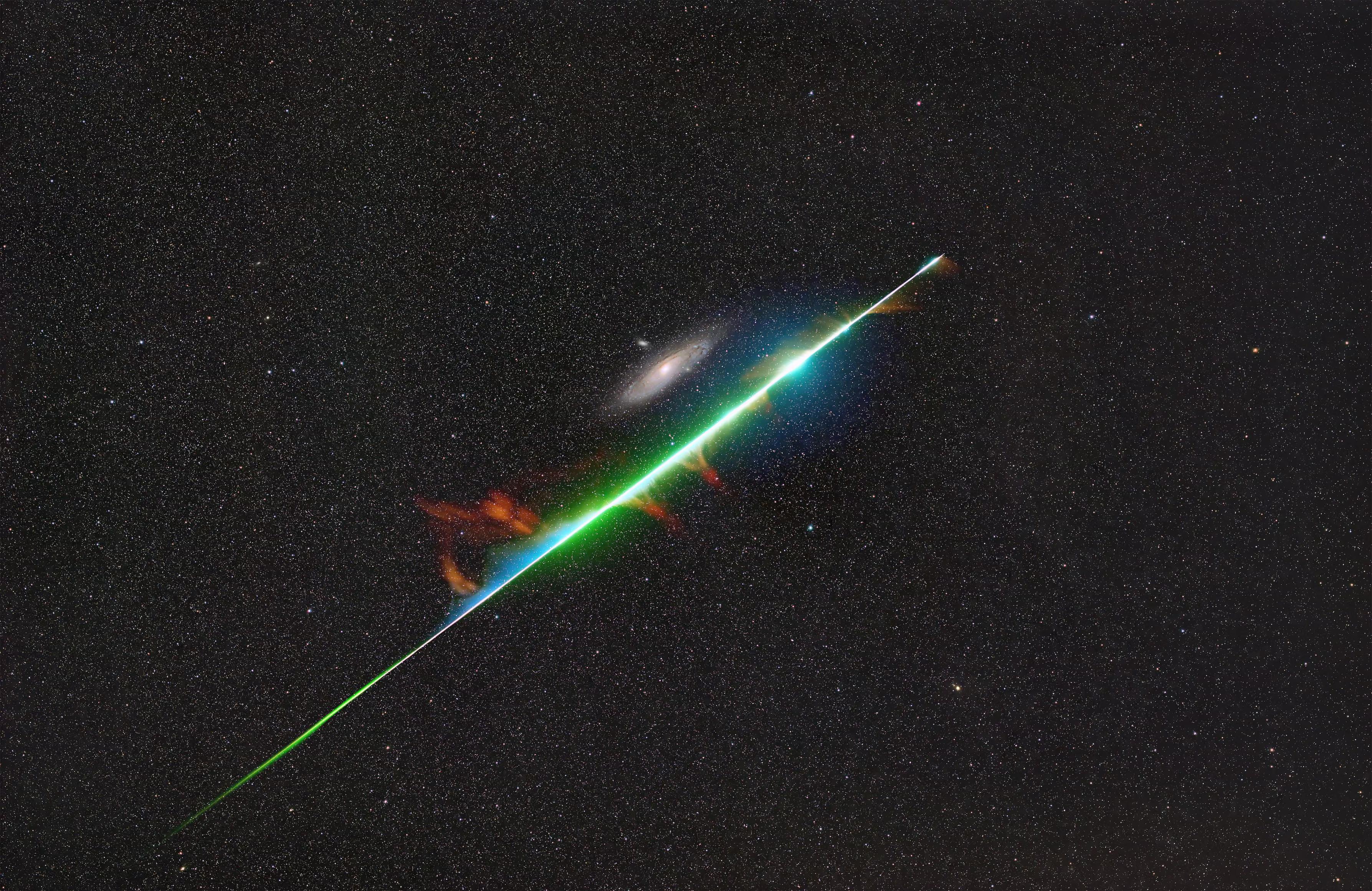 This photograph captures a lucky moment when a brilliant fireball from the Perseid meteor shower appears to graze the Andromeda galaxy.