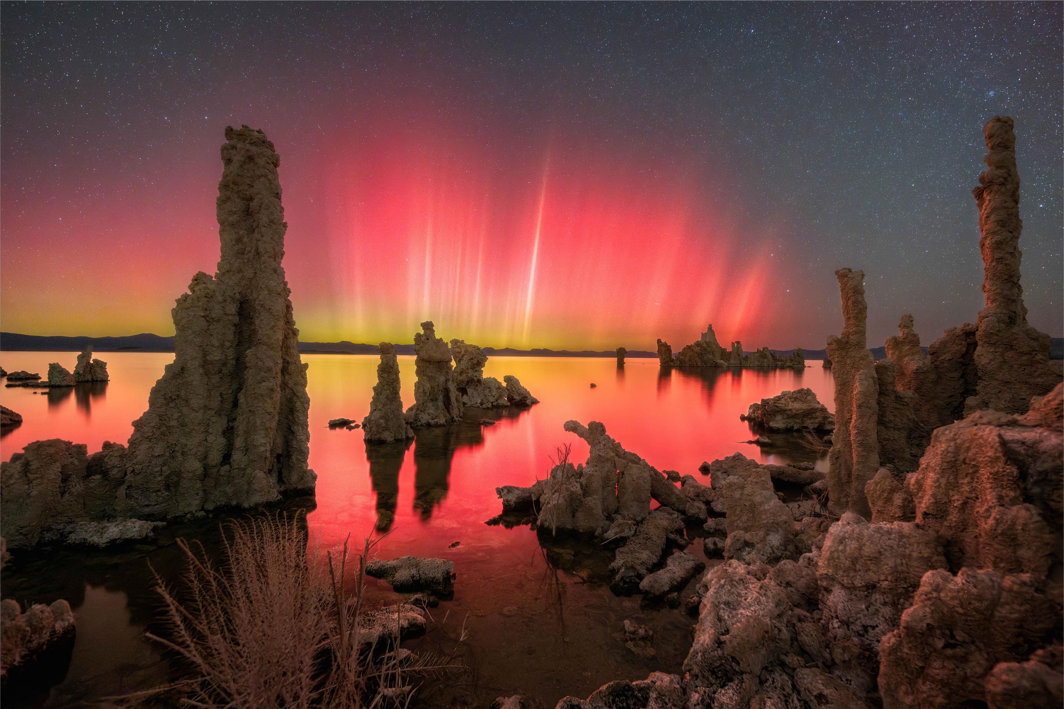 Vibrant ribbons of magenta and green light up the sky, reflecting in the still waters among the rock formations.