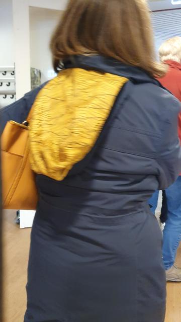 Mens op de rug gezien, met kleurige capuchon binnenstebuiten op donkerblauwe jas. Niet afgebeeld: mijn jeukende vingers.