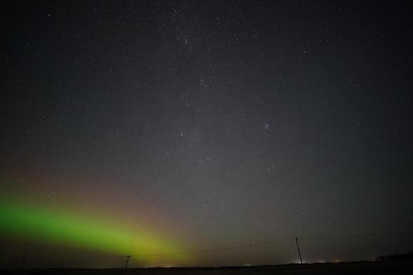 A band of green and red auroras off to the left side, with the band of the Milky Way stretching vertically across the picture