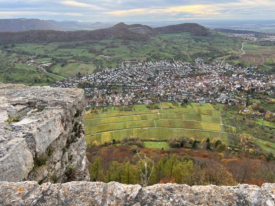 Das gleicher Panorama wie im vorigen Bild von der Burgruine Hohenneuffen Richtung Achalm im Querformat. Im Vordergrund der Ort Neuffen. Am Berghang davor Weinanbau