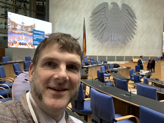 Selfie mit Alm und einem fetten Bundesadler an der grauen Rückwand hinter den Plätzen des ehemaligen Präsidiums