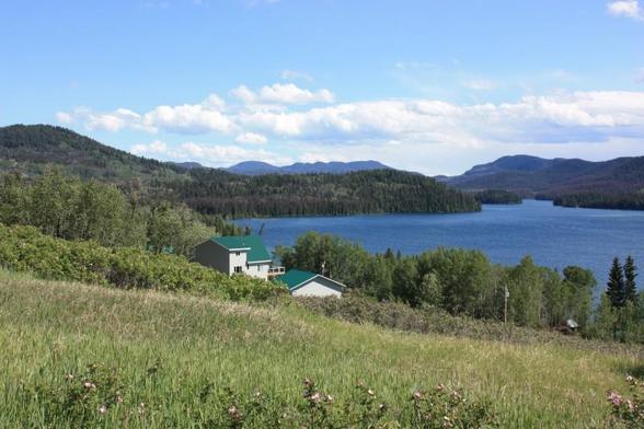 A sloping grassland leads to a blue lake that is surrounded by tree-covered hills and backed by mountains.