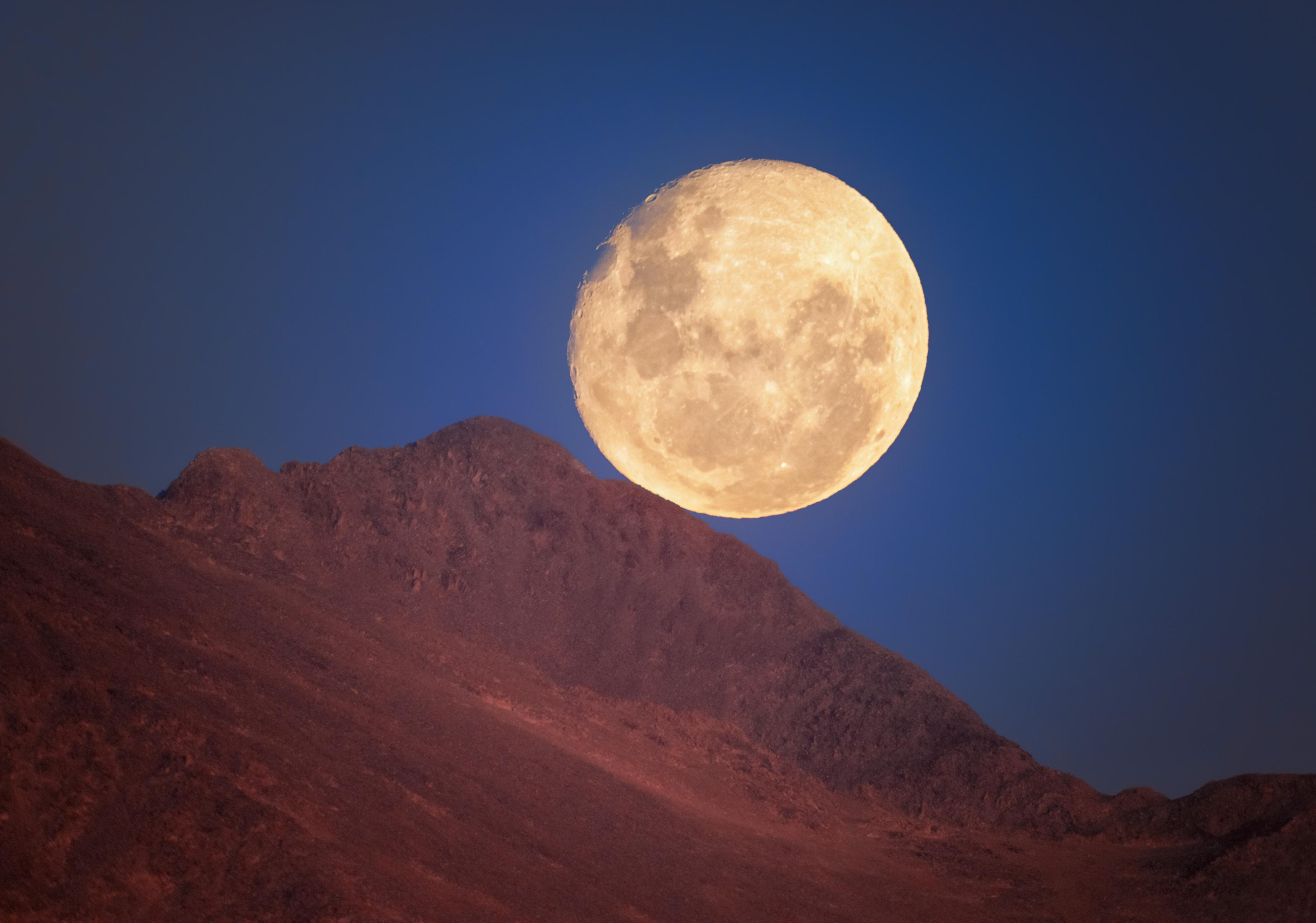 A gorgeous gibbous Moon rests above a ridge line near Cerro Pachón, the home of four NOIRLab-operated telescopes including NSF–DOE Vera C. Rubin Observatory; Gemini South, one half of the International Gemini Observatory, supported in part by NSF; and the SOAR Telescope of Cerro Tololo Inter-American Observatory, a Program of NSF NOIRLab.
The particular beauty of the Moon and its features are visible in this delightful image. The dark splotches of ancient, basaltic flats known as maria splatter across our satellite. These features formed when basalt moved from the lunar interior to fill basins on the surface during a time of active volcanism on the Moon. On the left side of the Moon, as seen from this perspective, are the two famous maria: Mare Tranquillitatis (immediately above center left) and Mare Serenitatis (center left). These maria, respectively, were the landing sites for the first and last human visits to the Moon.
On the upper left-hand edge of the Moon, the slopes and edges of the Moon’s other distinct feature, craters, appear starkly against the dark blue sky. One of the most distinct lunar craters, the massive Tycho crater, is in the upper right quadrant of the Moon in this image, flipped almost 180 degrees compared to the view from the northern hemisphere. Craters on the Moon are younger than the maria, and Tycho crater is particularly young, as evident by its sharp appearance.