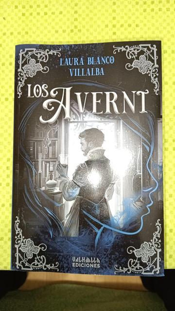Cubierta de «Los Averni». El título en letras historiadas, muy decimonónicas y encima el nombre de la autora. En blanco y negro, con toques azules, es la imagen de un joven de la época de espaldas, algo escorzado como para verle el rostro, con una copa con un líquido sospechoso en la mano. Está frente a una ventana en un laboratorio biblioteca. Superponiéndose a todo, incluso a cuatro adornos esquineros, la imagen de una joven esbozada con pocos trazos en azul.