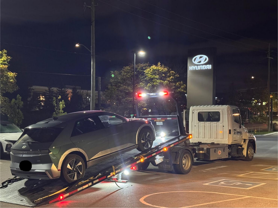 Hyundai Ioniq 5 on a flatbed tow truck being unloaded at a dealership at night.