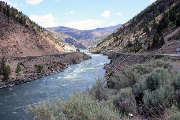 A rapid filled river runs between steep and bare banks from the hills and lakes in the distance.