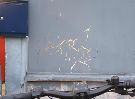 Met grijs dichtgeverfd raam, maar door de bliksemachtige barsten in de verf schijnt het kunstlicht van binnen door.