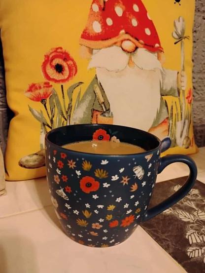 A cup of coffee in a navy mug with orange, yellow, and white flowers...