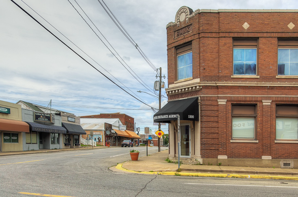 A quiet, small-town street corner features a brick building with a sign labeled "BANK" at the top