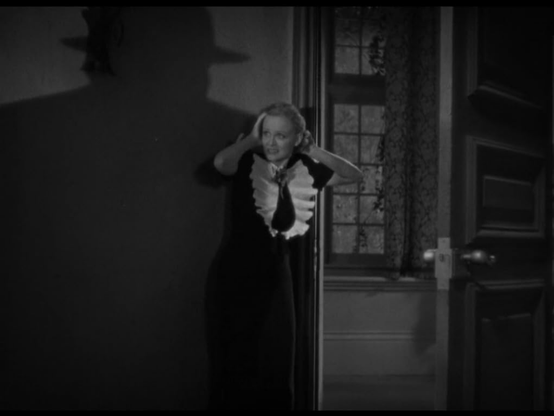 an image from the movie, the damsel screaming in a dark hallway, a shadow of a large figure wearing a hat is looming in and large , cast over the wall onto her, she is recoiling in horror