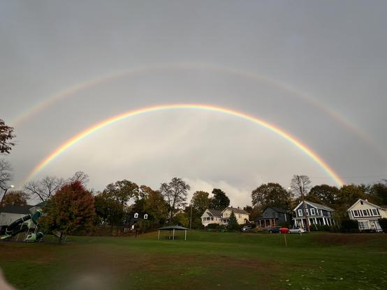 a very bright double rainbow, the entire arc is visible over a neighborhood park, and a row of houses behind the park. The inner arc is very bright, above it is a thick band of gray, then the 2nd rainbow above it, fainter than the lower one. Fantastic display! 