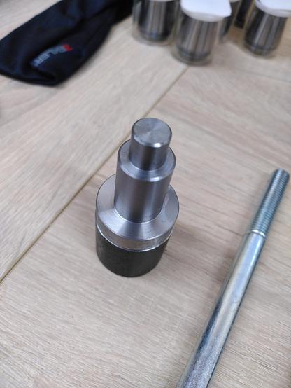 A turned metal part next to a bolt. Both are shiny. One due to its zink plating the other due to some most excellent work on a lathe.