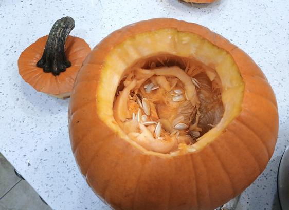 A top view of a pumpkin shows the area around the stem removed and all three pulp and seeds inside waiting to be removed