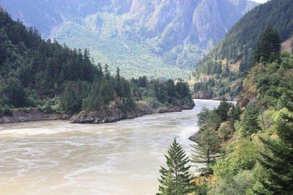 The whirlpool filled Fraser River flows around a sharp rocky bend in the river bed, on its way from the high hills in the background.