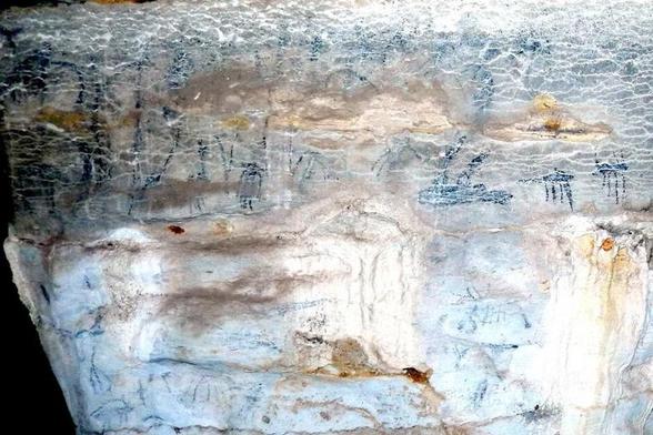 Cueva con dibujos negros variados en sus muros, algunos que parecen dioses egipcios y otros son líneas en zigzag.