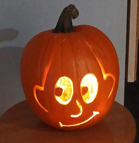 A pumpkin sits on a stool, and it has a cartoon face carved in it

It's slightly reminiscent of a  minor Groening Futurama character.