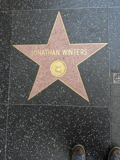 Hollywood Walk of Fame star for Jonathan Winters with a television emblem, set in a speckled black terrazzo sidewalk and shoes partly visible.
