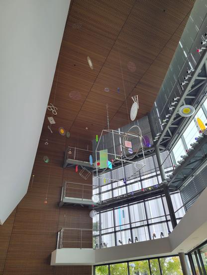Daytime interior photo of sculpture art "Fertile Ground" by Cork Marcheschi. Various electic items hang from the ceiling in various geometric shapes and objects (e.g., eyeglasses, plates, wire-frame cubes, rectangles).