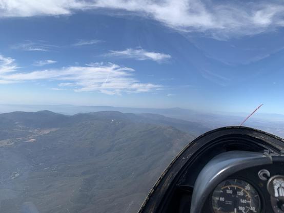 Aerial view from a glider of a mountain on a sunny day, with a white observatory dome visible in the distance