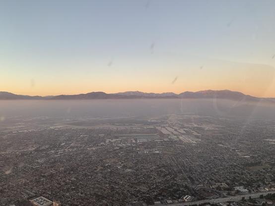 At dusk, an aerial view of drawling suburbs below haze, with a mountain range in the distance