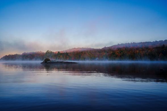 A close view of a calm lake with a misty surface and autumn trees on the shore, creating a serene atmosphere.