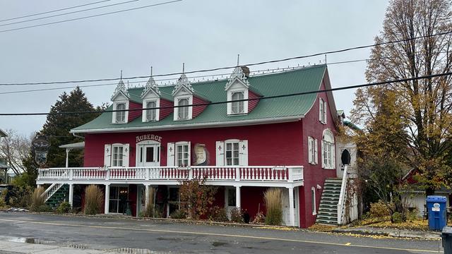 Die «Auberge Mange-Grenouille». Ein altes, dreigeschossiges  Gebäude mit roten Backsteinen, grünem Giebeldach und weissen Fensterumrandungen bzw. weissem Balkon.