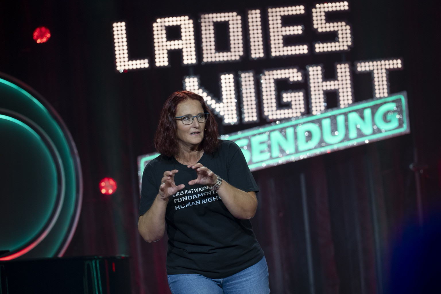 Rothaarige lustige Frau auf Bühne mit Deko von 100. Folge Ladies Night