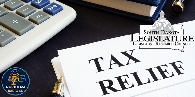 Calculator, pen, and papers labeled "TAX RELIEF" on a desk. South Dakota Legislature logo; Northeast Radio SD logo. Office setting.