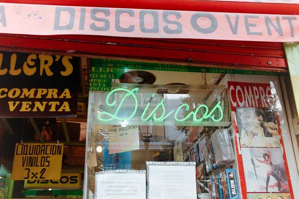 Photograph of a neon sign with the word "Records" in the window of a record store. Other signs and the store's awning can be seen around it.

Fotografía de un neón con la palabra "Discos" en el escaparate de una tienda de discos. Alrededor se ven otros carteles y el toldo de la tienda. 