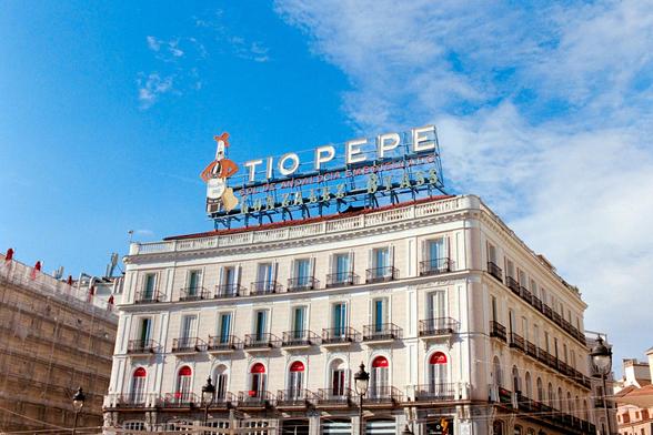 Photograph of the iconic Tío Pepe advertisement in Puerta del Sol in Madrid with a blue sky, partially covered with clouds.

Fotografía del icónico anuncio de Tío Pepe en Puerta del Sol en Madrid con el cielo azul, cubierto parcialmente de nubes.