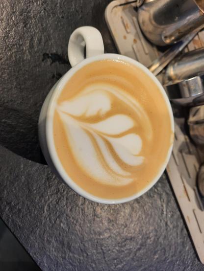 Kopje koffie met latte-art-poging tot een tulp in een witte tas.