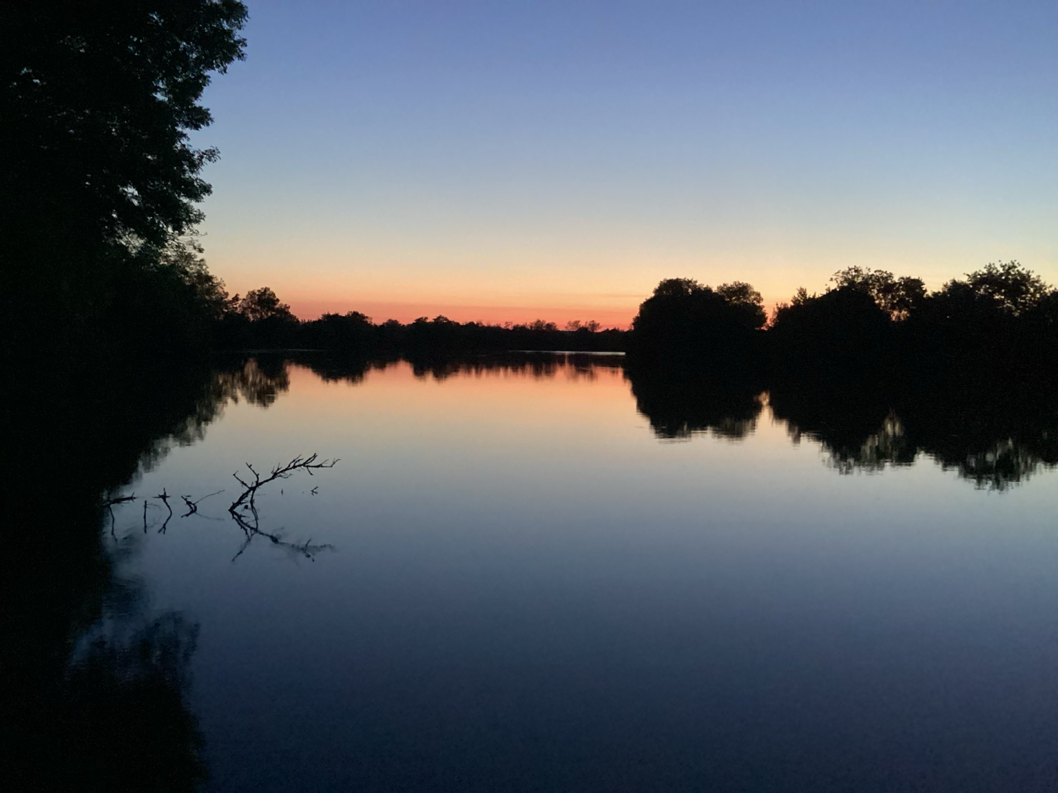 Flusslandschaft im Abendrot. Bäume und Sträucher sind schon schwarz und spiegeln sich im Fluss.