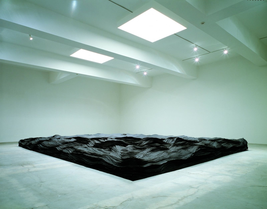 View 1: The sculpture is an aggregation of hundreds of thousands of brown tar paper strips, stacked at varying heights and widths to suggest an undulating landscape or ocean waves. 