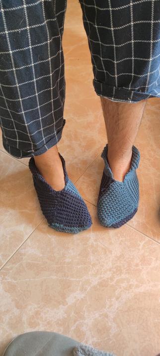 Vista frontal de una persona con pantalones de cuadros azules y pantuflas tejidas a mano en dos tonos de azul, parada sobre un suelo de cerámica clara.