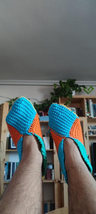 Vista frontal de unas pantuflas tejidas de forma artesanal en tono azul, turquesa, amarillo y naranja.