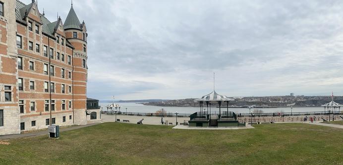 Links ein Teil des Château Frontenac. In der Mitte Rasen/Terrasse und unten der Sankt-Lorenz-Strom. Der Himmel ist grau.