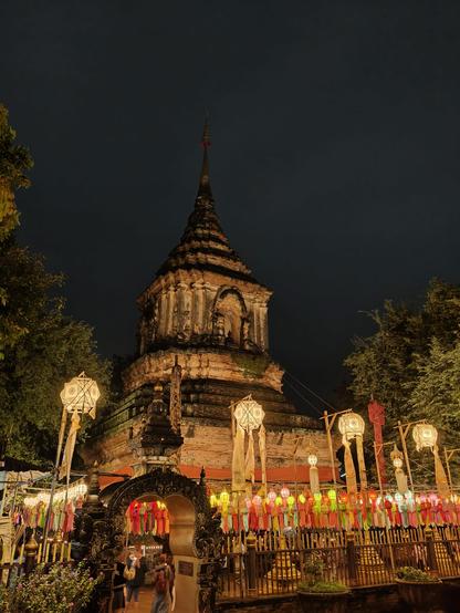 The photo captures a Buddhist temple in Chiang Mai, illuminated at night. The scene is decorated with numerous glowing lanterns of various sizes and colors, suggesting it was taken during a festival like Loy Krathong or Yi Peng.
