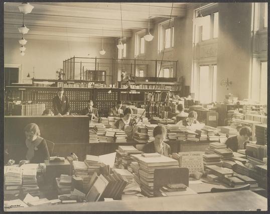 Librarians classifying books at the Library of Congress, Washington, D.C. (LOC)

The Library of Congress from Washington, DC, United States 

The image shows a number of librarians actively engaged in processing library material in a space within the Library of Congress in Washington, D.C. The room appears to be a large, well-lit working area. Long tables, shelving units and stacks of books and bound volumes are visible. 

The librarians seem to be engaged in classification, cataloguing and shelving tasks — handling books, perhaps checking index cards or labels, and placing the volumes in their correct place.

https://commons.wikimedia.org/wiki/Category:Librarians#/media/File:(Librarians_classifying_books_at_the_Library_of_Congress,_Washington,_D.C.)_(LOC)_-_Flickr_-_The_Library_of_Congress.jpg