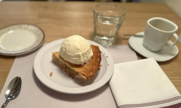 Ein kleiner Teller mit einem grossen Stück gedeckten Apfelkuchen. Darauf eine sehr grosse Kugel Vanilleeis.