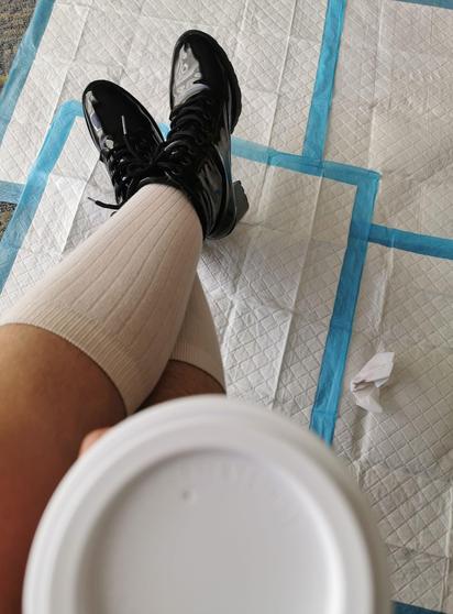 Soledad Domina sits in knee high cotton socks that lead to her black heeled boots, so shiny that they reflect daylight from a window. She holds in one hand a coffee cup, and below her lies a neat arrangement of absorbent pads, sometimes used in toilet play. On the pads sits one tidy crumpled tissue.