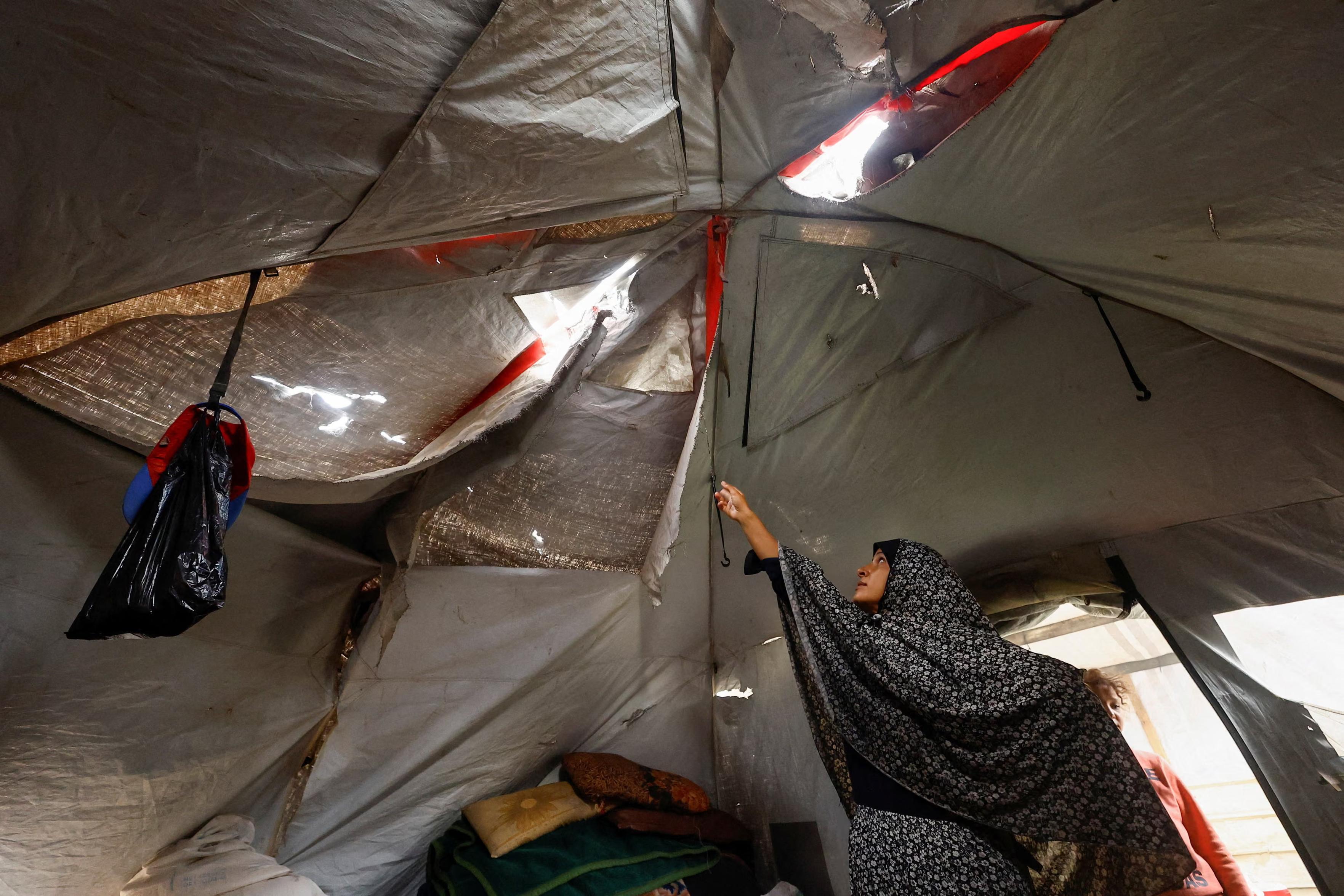 A displaced Palestinian woman shows her torn tent.