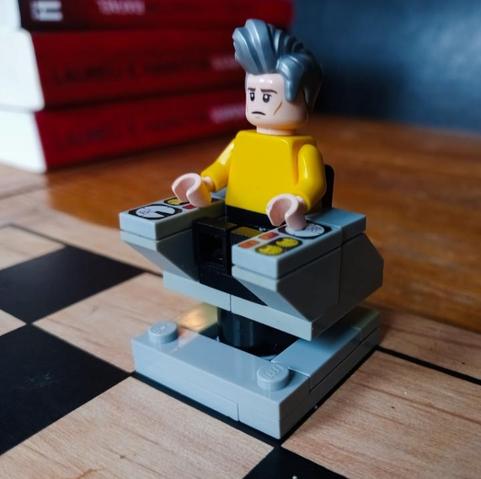 A LEGO Captain Pike, sitting in his command chair, in the King's position on a wooden chessboard