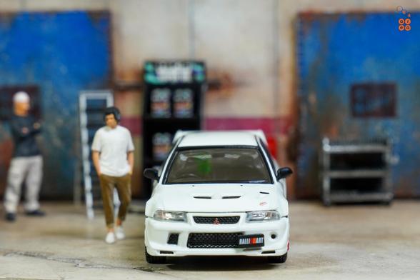 A front side of Mitsubishi Lancer RS Evolution 6, Monte Carlo Edition, Scortia White by Hobby Japan in 1:64 scale with 1:64 figures on AREA 164.