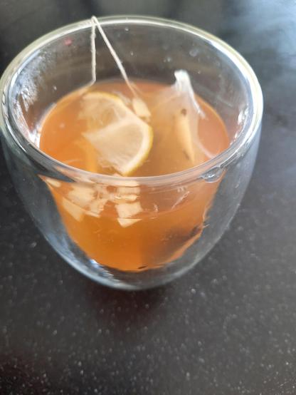 Een glas groene thee met honing, schijfjes limoen en gember in een doorzichtige mok, bedoeld als natuurlijke remedie bij verkoudheid of griep.