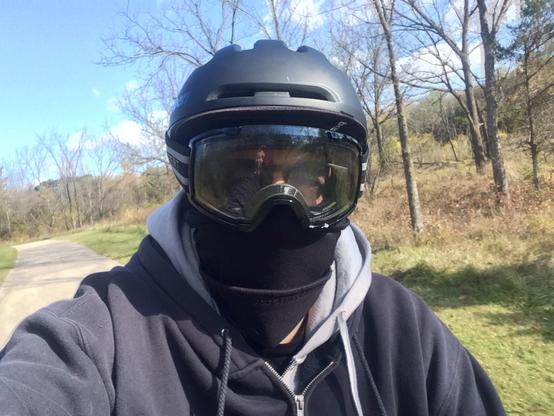 A human person wearing a bike helmet, goggles, and a balaclava, while riding a bike.