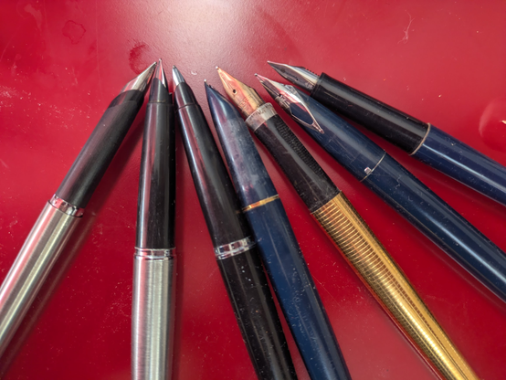 A bunch of quite old fountain pens, caps removed to expose the nibs.